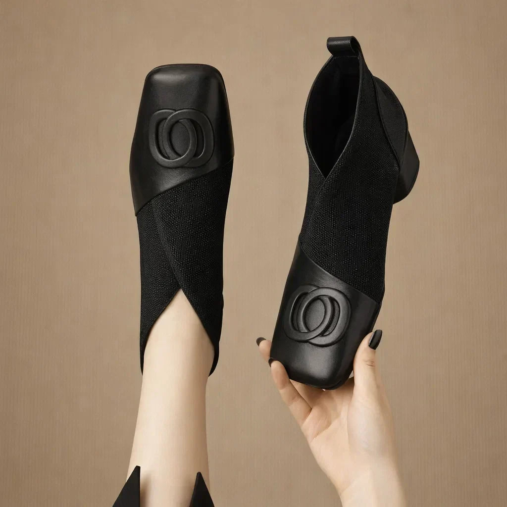 Black square-toe ankle boots with elastic side panels and embossed circular logo detail