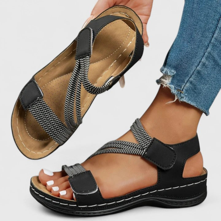Black cushioned wedge sandals with textured straps, adjustable side buckle, open toe